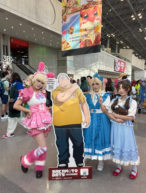 Cosplayers posing with the Sakamoto Days activated standee at a convention