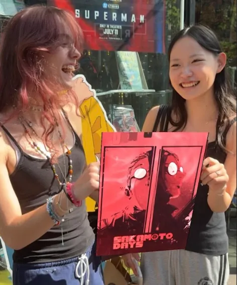 Two fans holding the activated Sakamoto Days poster